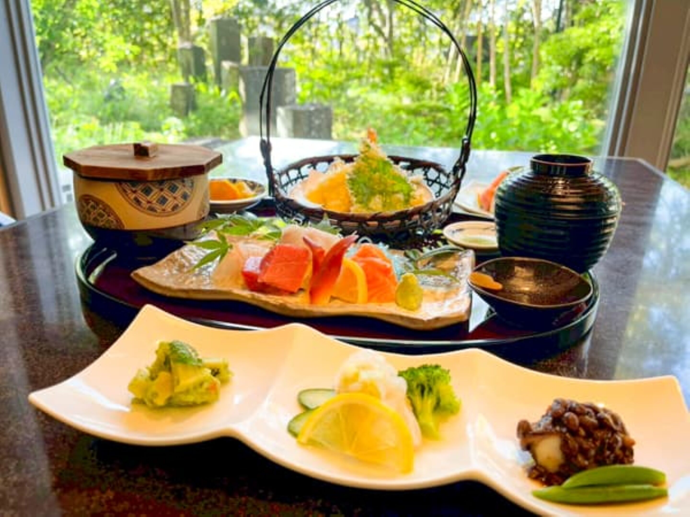 A table with various dishes, including sashimi, vegetables, and a bowl of soup.