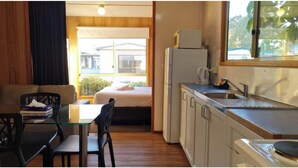 A compact room with a bed, a small table, a chair, a kitchenette, and a window with a view of buildings outside. - Discovery Parks - Mornington (Mornington)