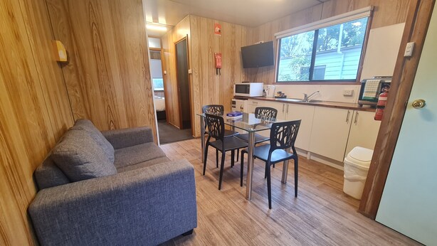 A compact living space with a sofa, dining table, chairs, a microwave, a small kitchenette, and a window. - Discovery Parks - Mornington (Mornington)