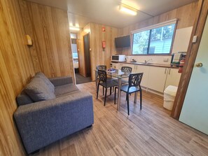 A compact living space with a sofa, dining table, chairs, a microwave, a small kitchenette, and a window. - Discovery Parks - Mornington (Mornington)