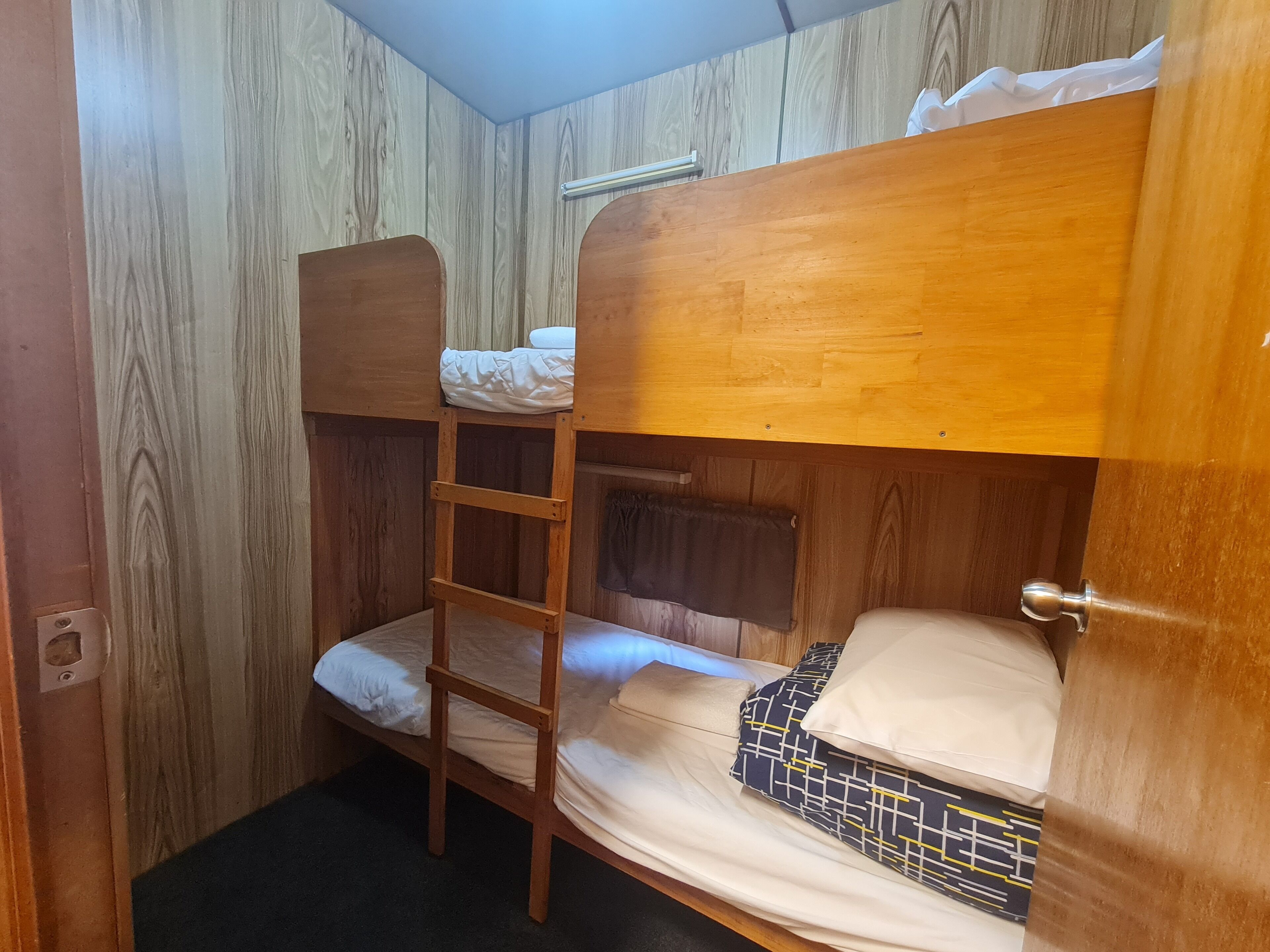 A bunk bed room with a wooden ladder, a small window, and a door.