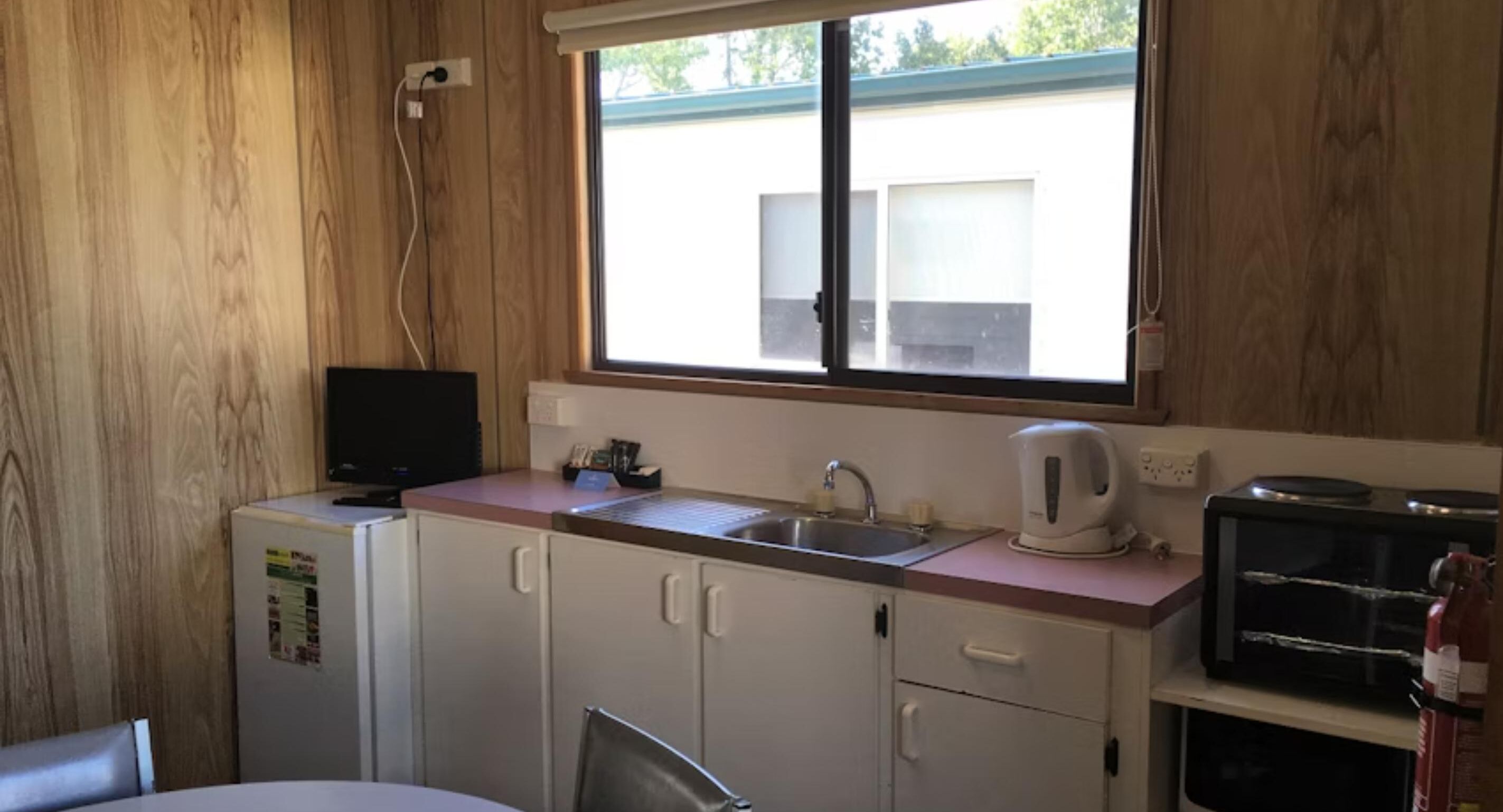 Una kitchenette compacta con ventana, un lavamanos, un hervidor y un refrigerador.