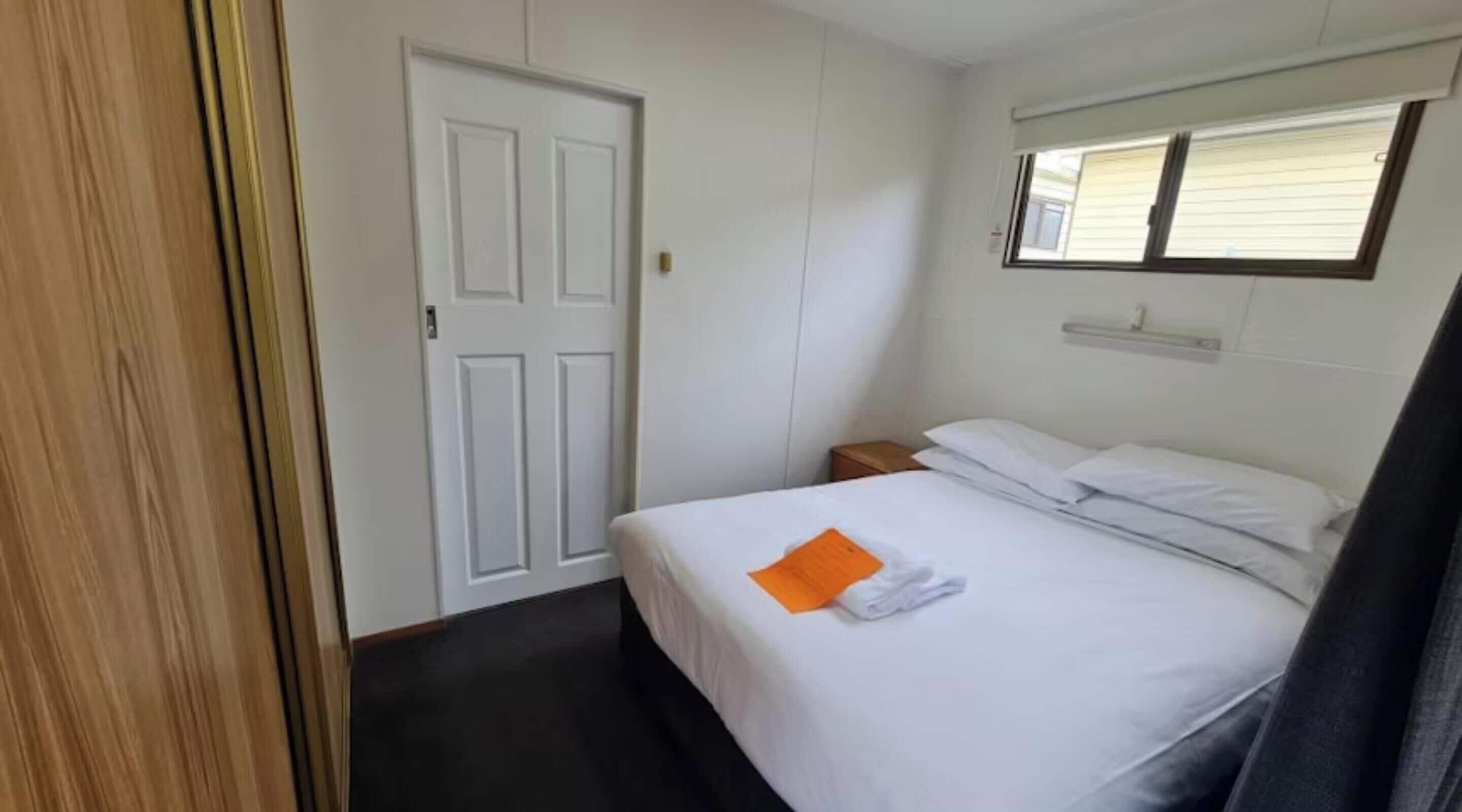 A hotel room with a bed, a nightstand, a white door, and a window with blinds.