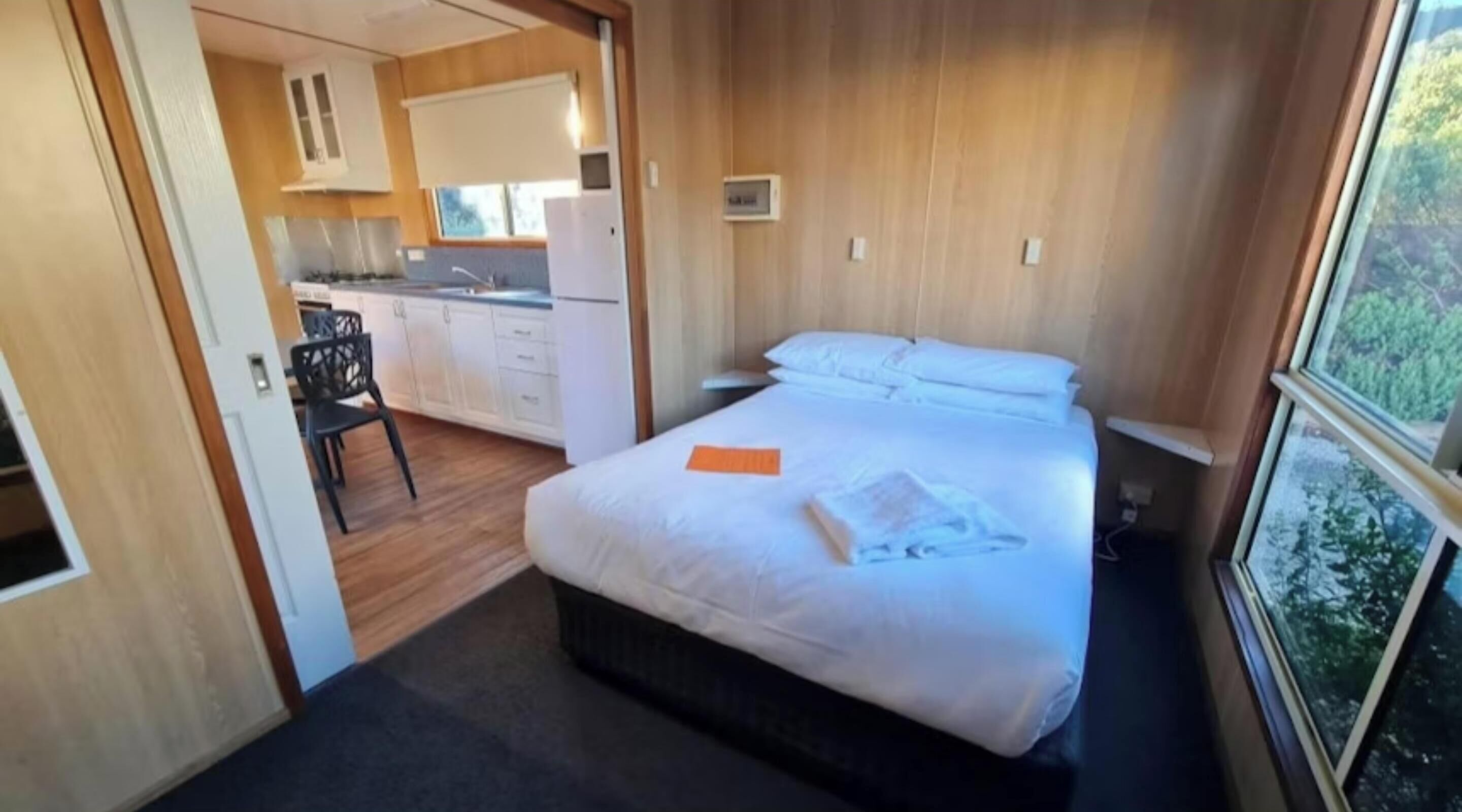 Un dormitorio con cama, escritorio y silla. Se ve una ventana con vistas a árboles.