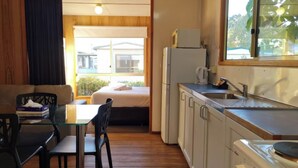 A compact room with a bed, a small table, a chair, a kitchenette, and a window with a view of buildings outside. - Discovery Parks - Mornington (Mornington)
