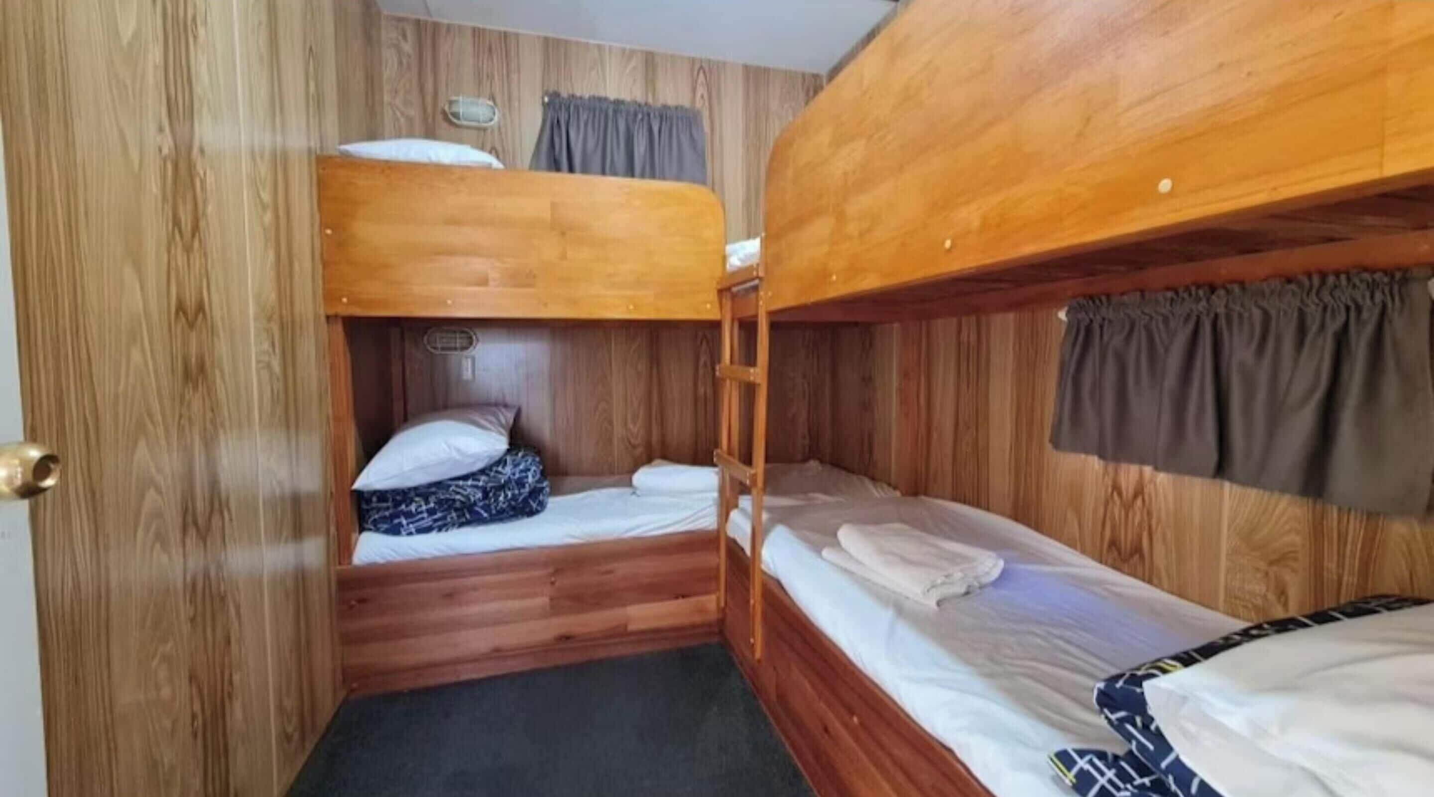 A compact cabin with two bunk beds, wooden walls, a small window with curtains, and a door.