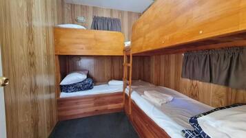 A compact cabin with two bunk beds, wooden walls, a small window with curtains, and a door.