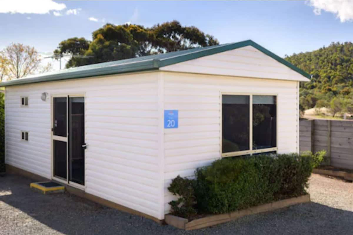 A small, single-story mobile home with a green roof, a number '20' sign, and a small garden area.