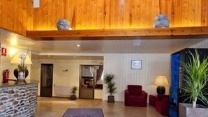 A lobby with a stone reception desk, wooden ceiling beams, red seating, and potted plants. - Residencia Daina (Arinsal)
