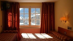 A hotel room with two beds, a window with a view of mountains, a radiator, and a wall-mounted lamp. - Residencia Daina (Arinsal)