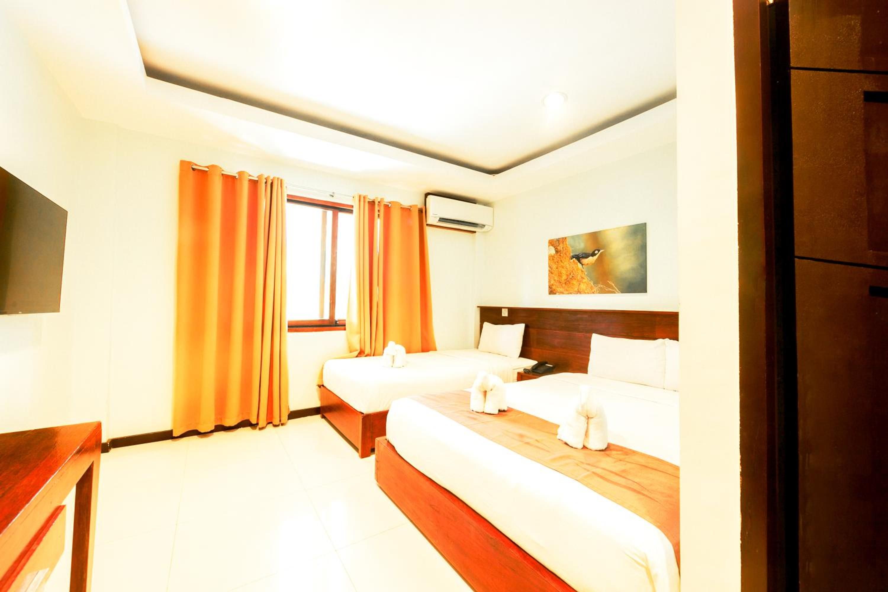 A hotel room with two beds, a flat-screen TV, an air conditioning unit, and a painting on the wall.