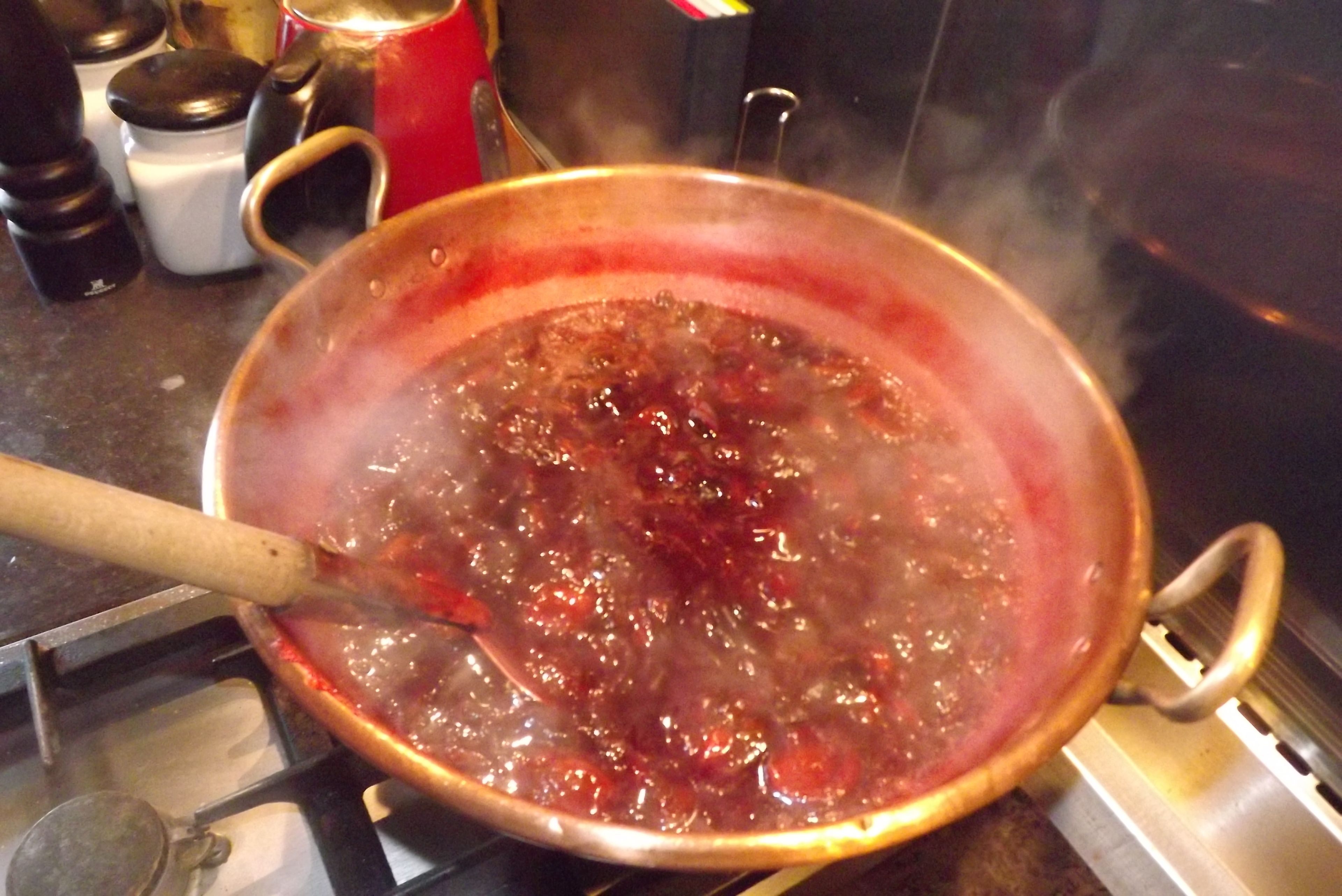 A pot on a stove with a wooden handle, boiling liquid, and steam rising.