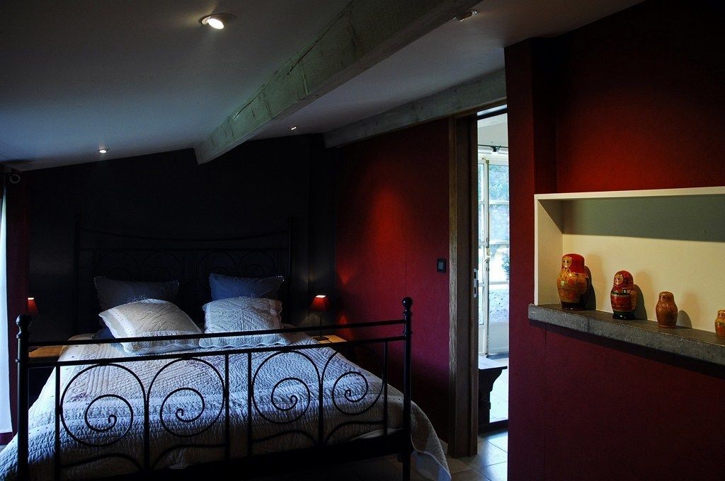 Une chambre à coucher avec un lit en métal, un mur rouge et une étagère ornée d’objets décoratifs.