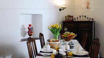 A dining table set with breakfast items, a vase of yellow flowers, and a fruit bowl.