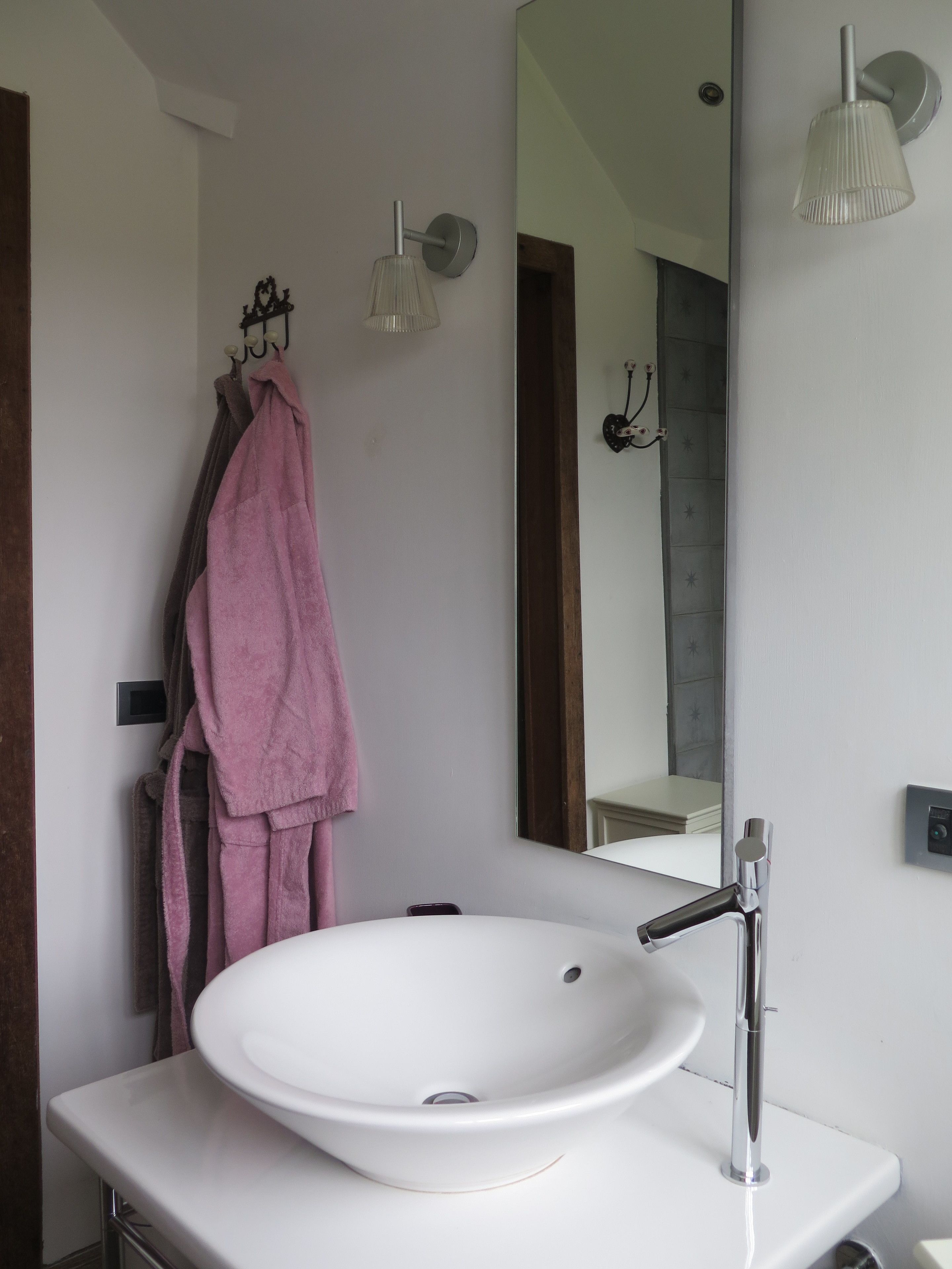 Une salle de bain avec un lavabo blanc, un miroir et un porte-serviettes sur lequel est posée une serviette rose.