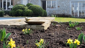 A stone house with a well-maintained garden featuring yellow flowers and a stone planter. - La Buissonnière (Ferrieres)