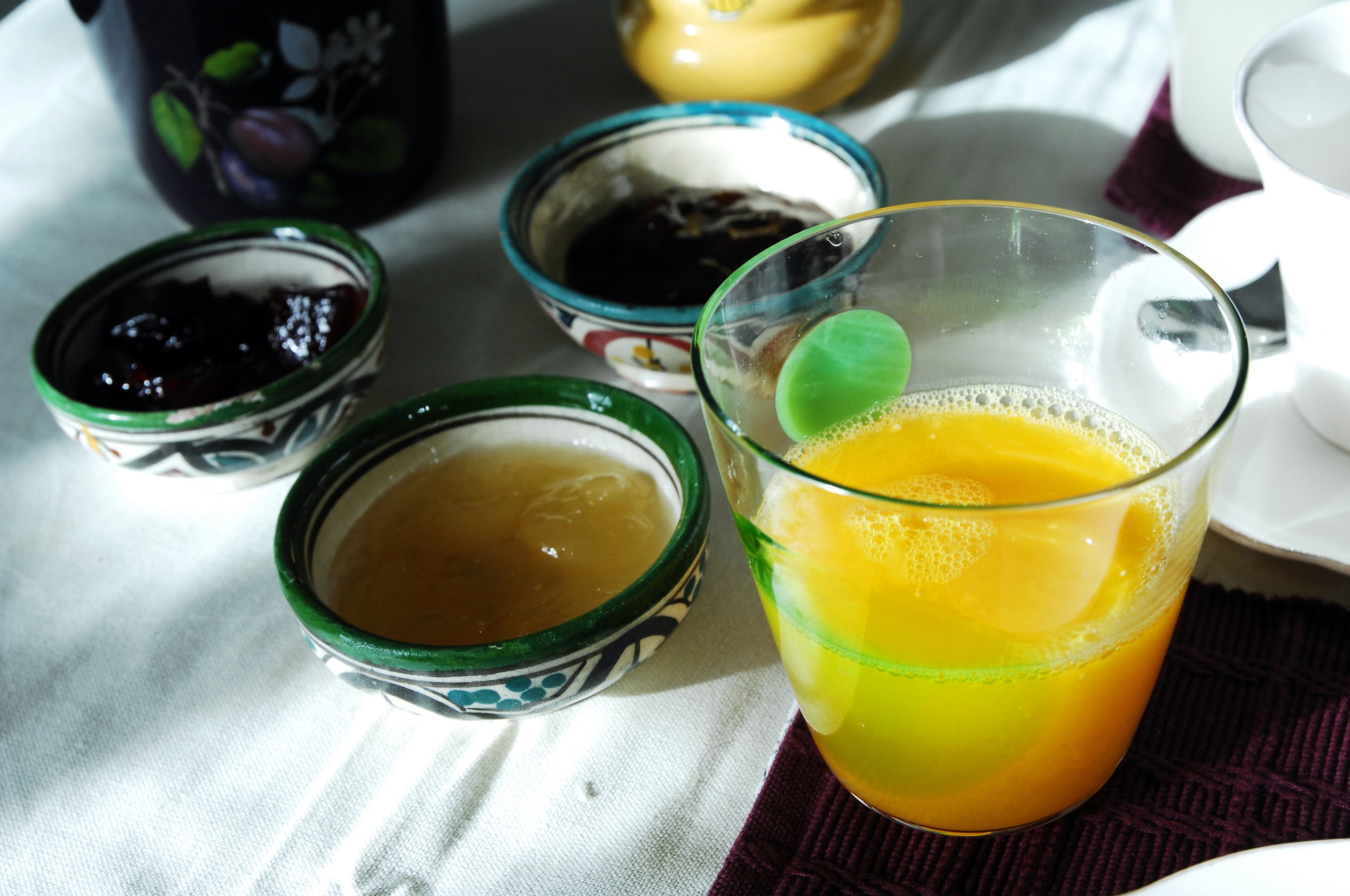 A table with a glass of orange juice, two small bowls with different liquids, and a decorative container in the background.