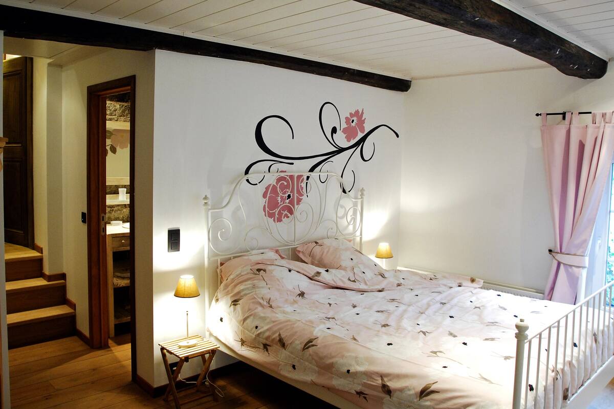Un dormitorio con cama, escalera de madera y un detalle decorativo en la pared.
