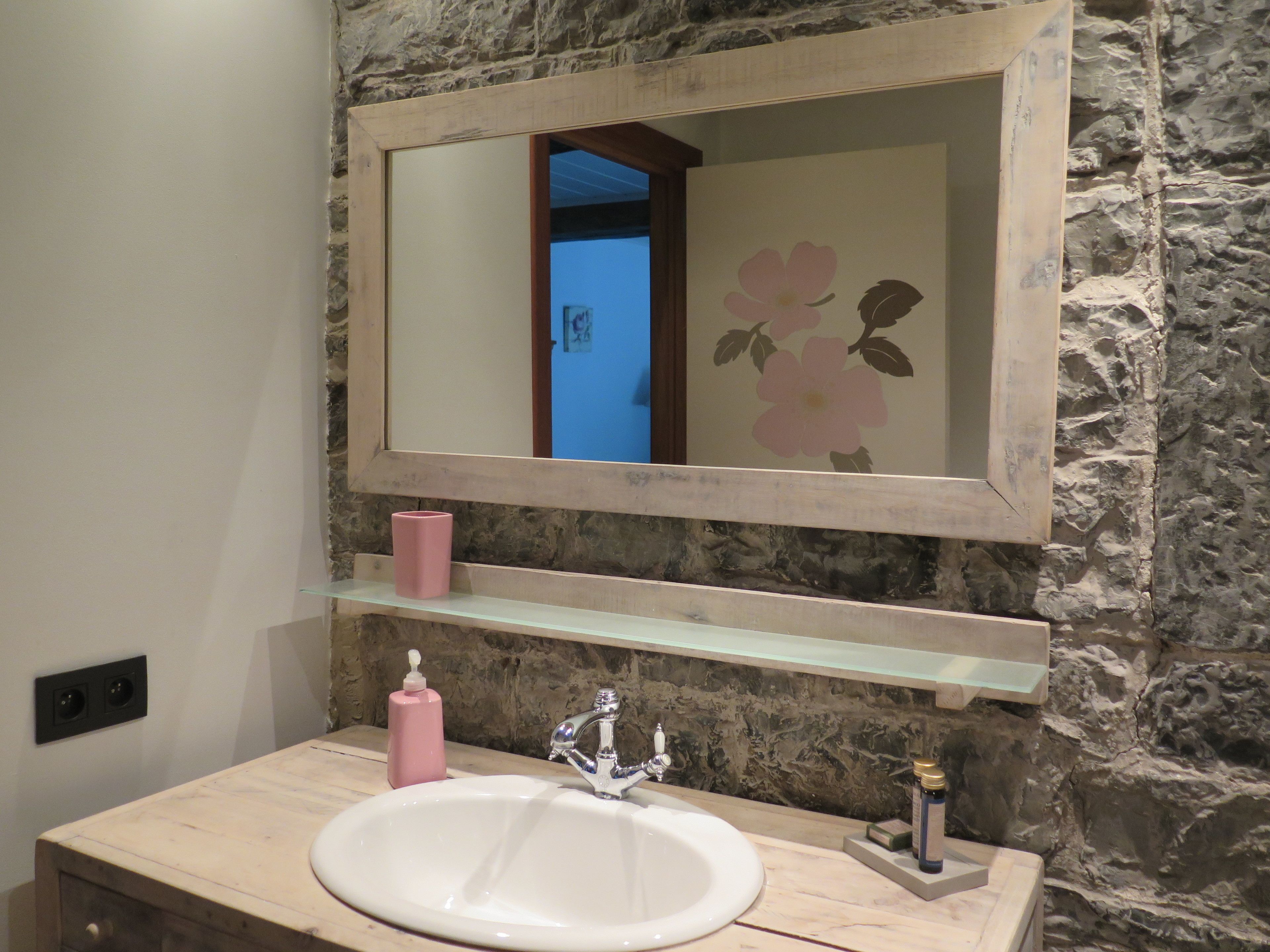 Une salle de bain avec un mur en pierre, un lavabo blanc, un miroir et un distributeur de savon rose.