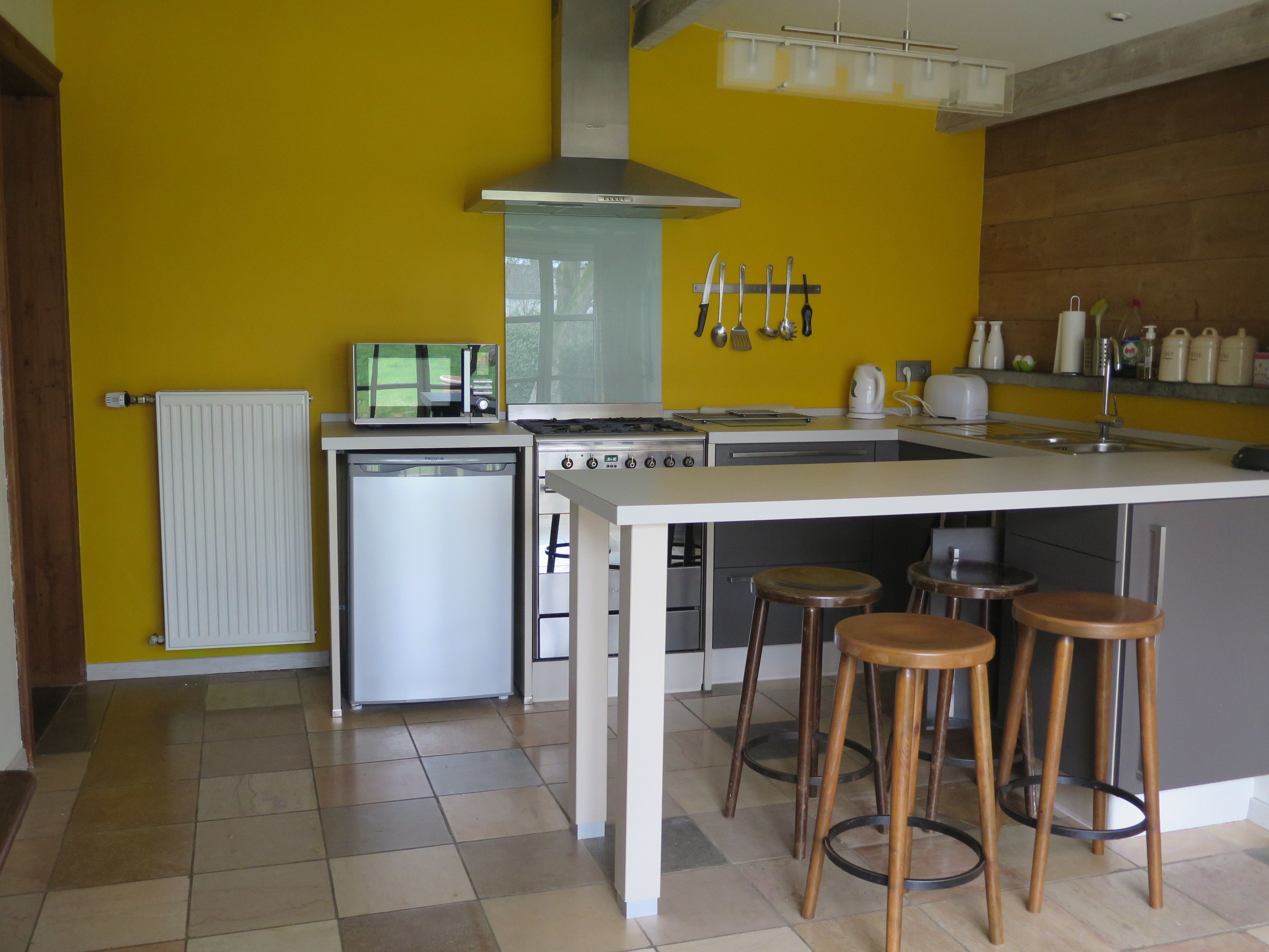 A modern kitchen with a central island, stainless steel appliances, and a yellow accent wall.