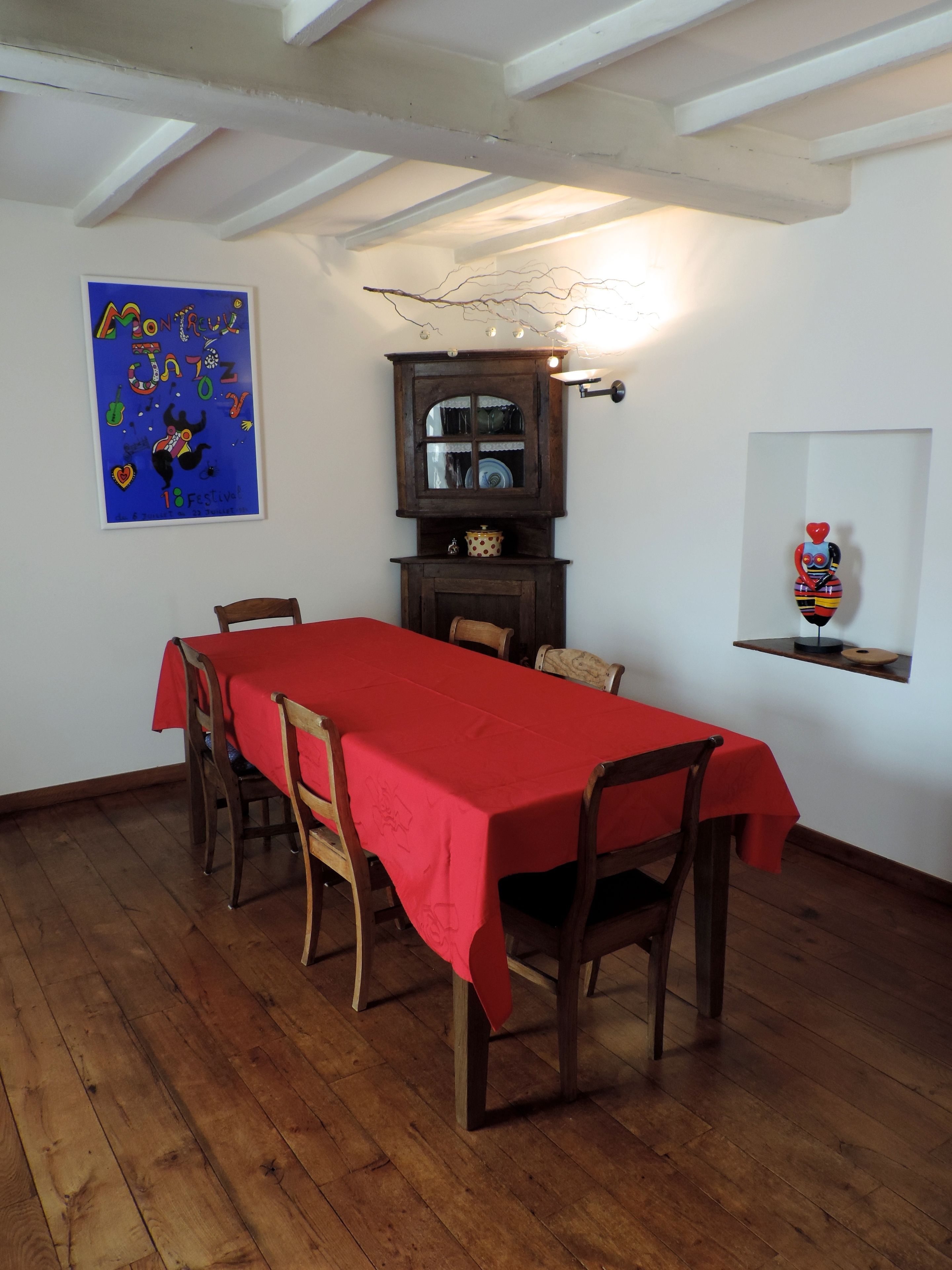 Une salle à manger avec une nappe rouge, des chaises en bois, un buffet en bois et une étagère murale agrémentée d’un objet décoratif.