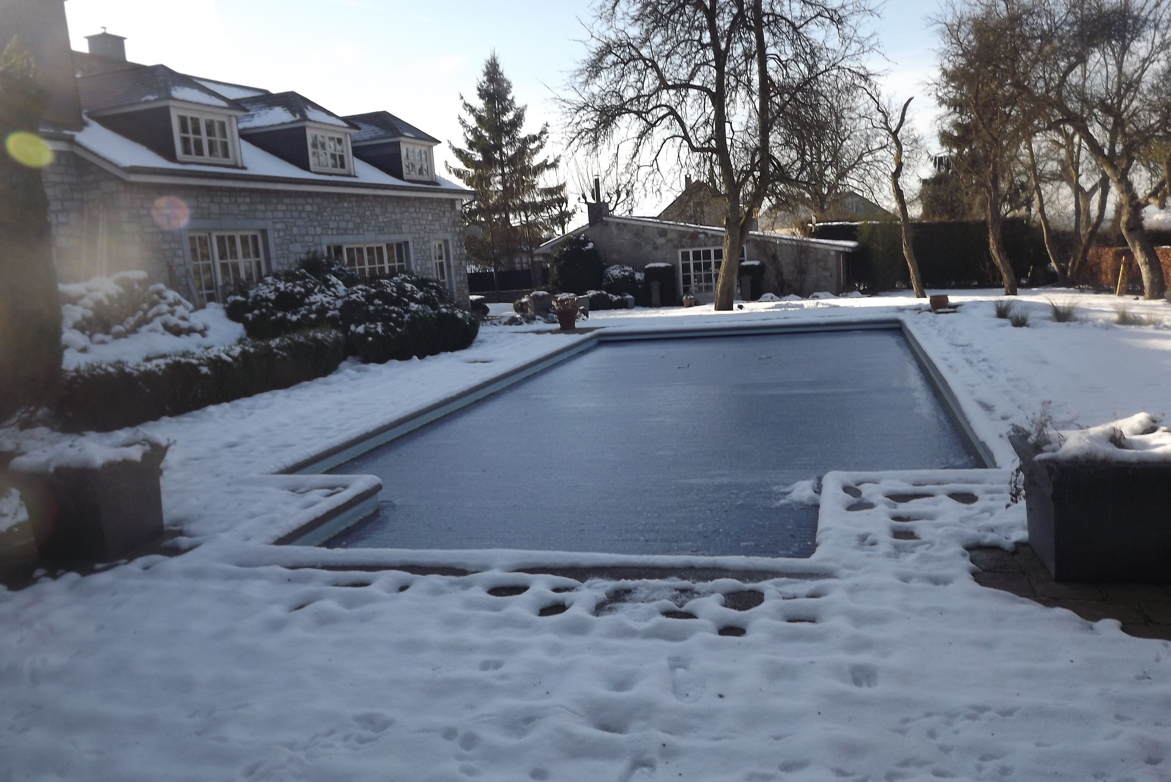 Een met sneeuw bedekte zwembad met een stenen huis op de achtergrond.