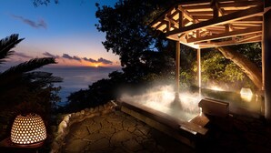 A hot spring area with a wooden pergola, stone flooring, and a view of the sunset over the ocean. - Kissho CAREN (Higashiizu)