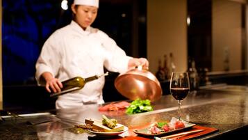 A chef preparing food in a kitchen with a copper pot and a wine glass on the counter.