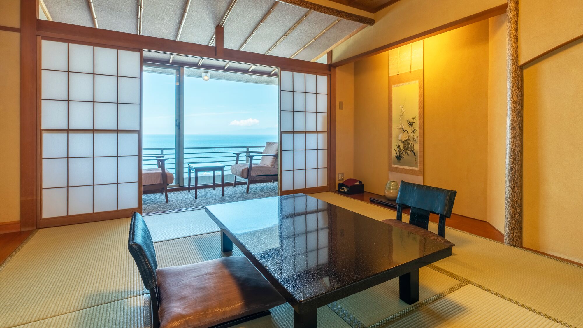 A tatami room with a low table, a bench, and a view of the sea.