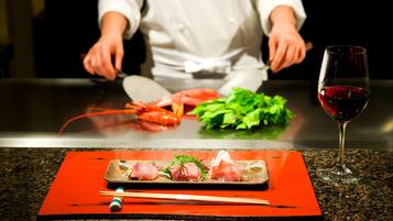 A chef preparing food at a counter with a plate of sashimi and a glass of red wine.