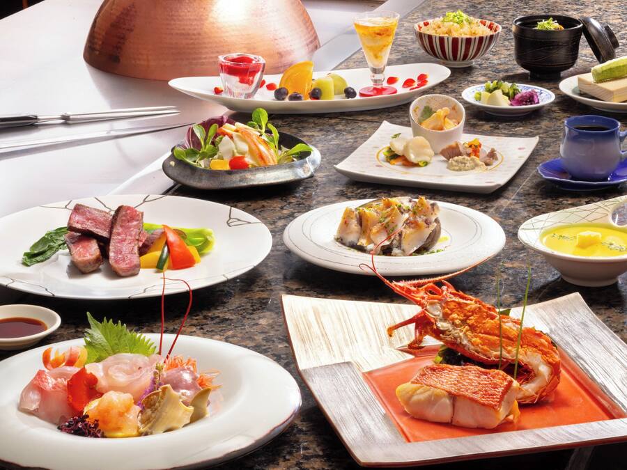 Diversos pratos em uma mesa, incluindo frutos do mar, legumes e um lagosto.