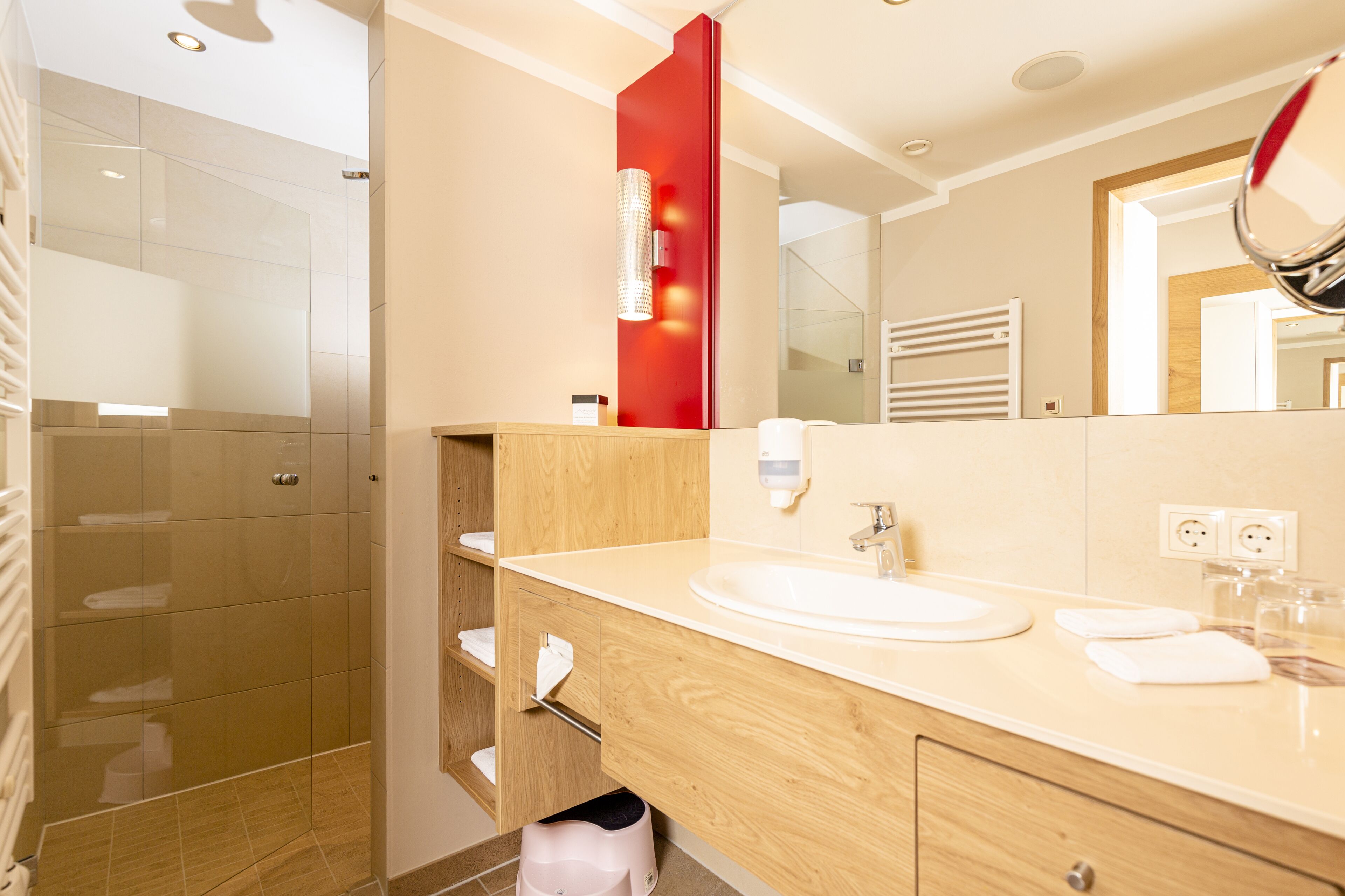 A modern bathroom with a wooden vanity, a large mirror, and a glass shower enclosure.