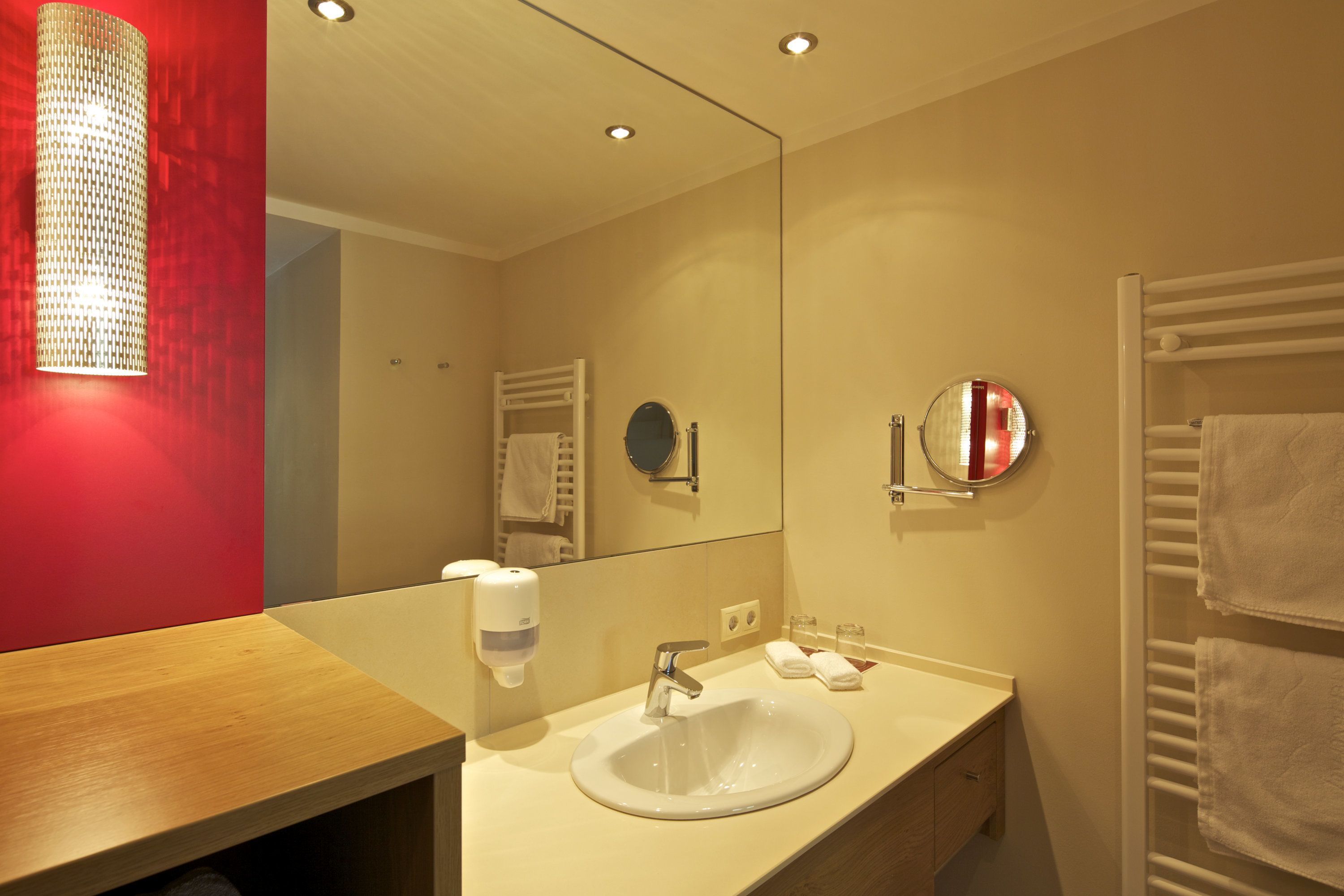 Baño de hotel con lavamanos, espejo, toallero y dispensador de jabón.