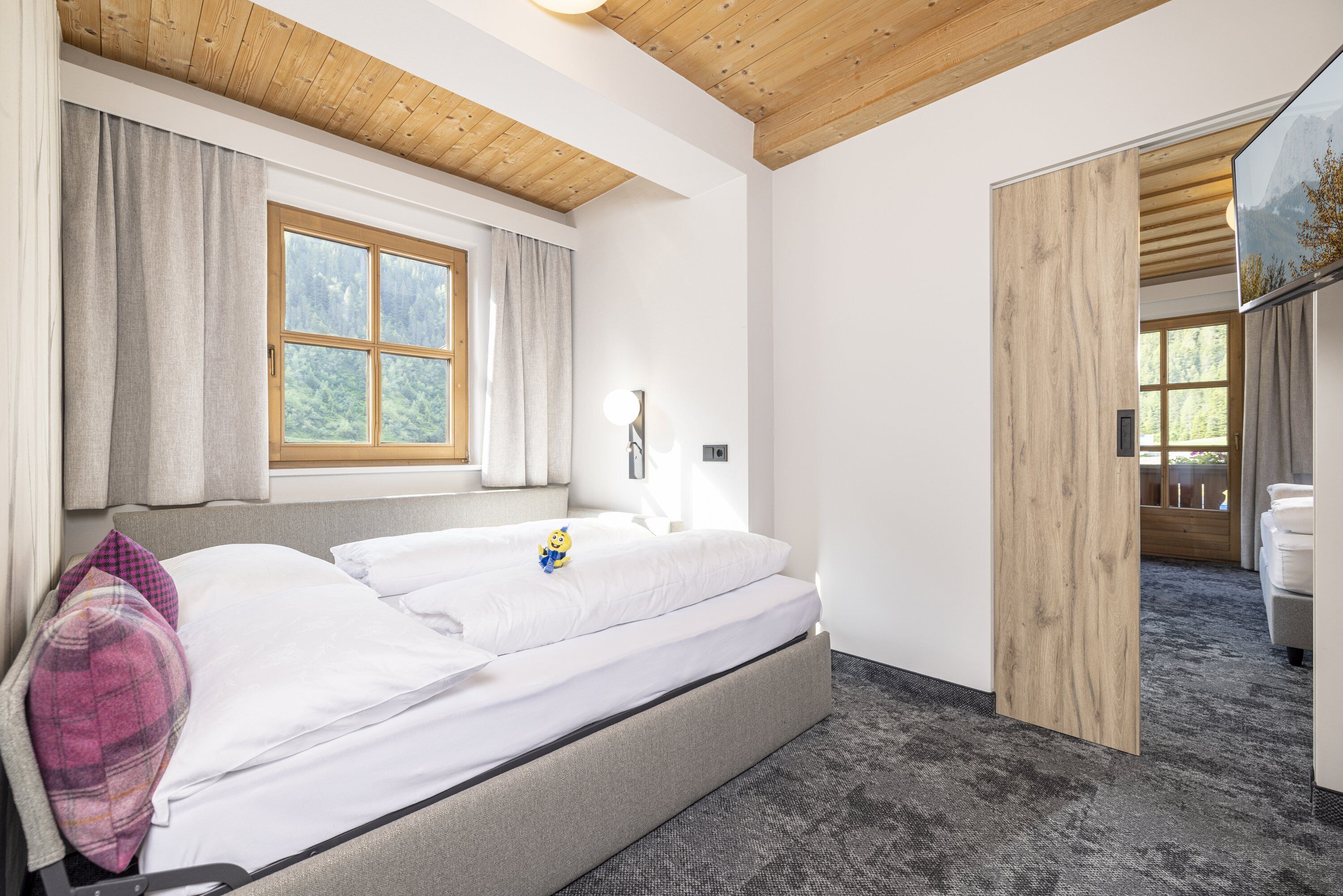 A modern bedroom with a bed, a window, and a wooden ceiling.
