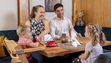 Een gezin aan een houten tafel, met een vaas gedroogde bloemen, een kaars en een placemat.