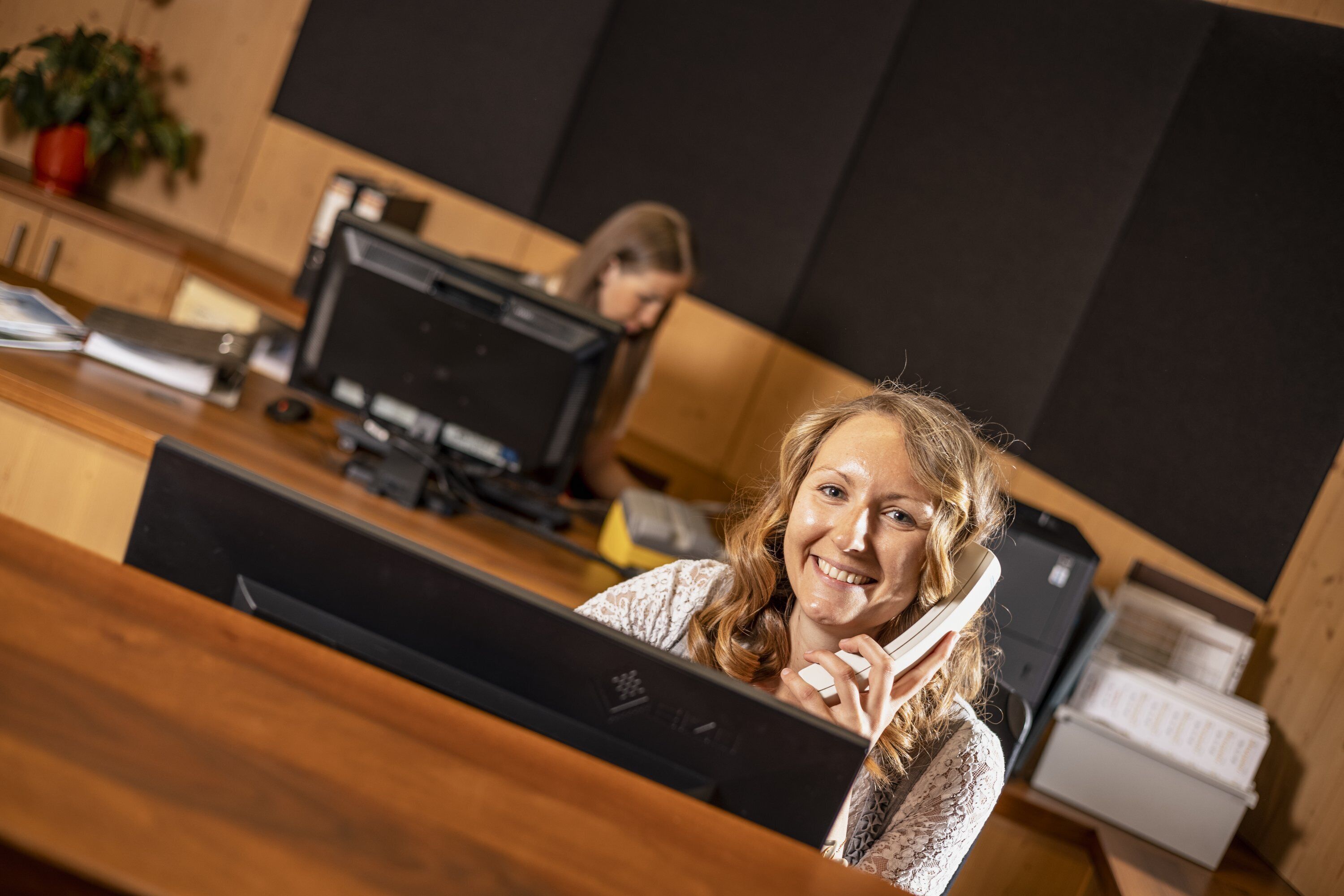 Iemand zit aan een bureau met een computer, een printer en een plant op de achtergrond.