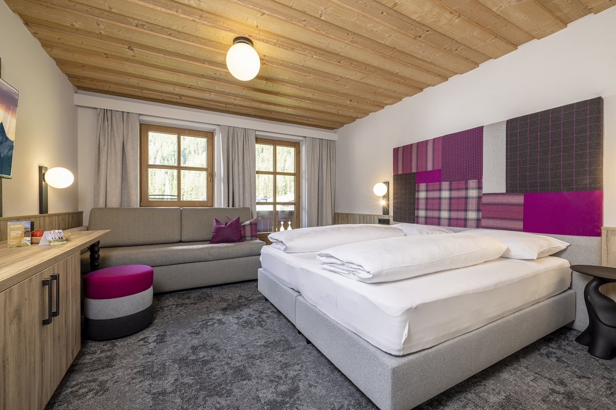 Un dormitorio con cama, escritorio, silla y ventana con cortinas.