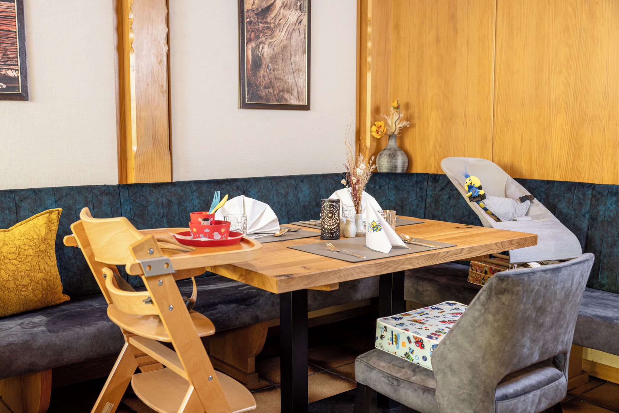 Un coin repas avec une table en bois, des chaises et un banc. La table est décorée de divers objets et un vase contenant des fleurs séchées y est posé.