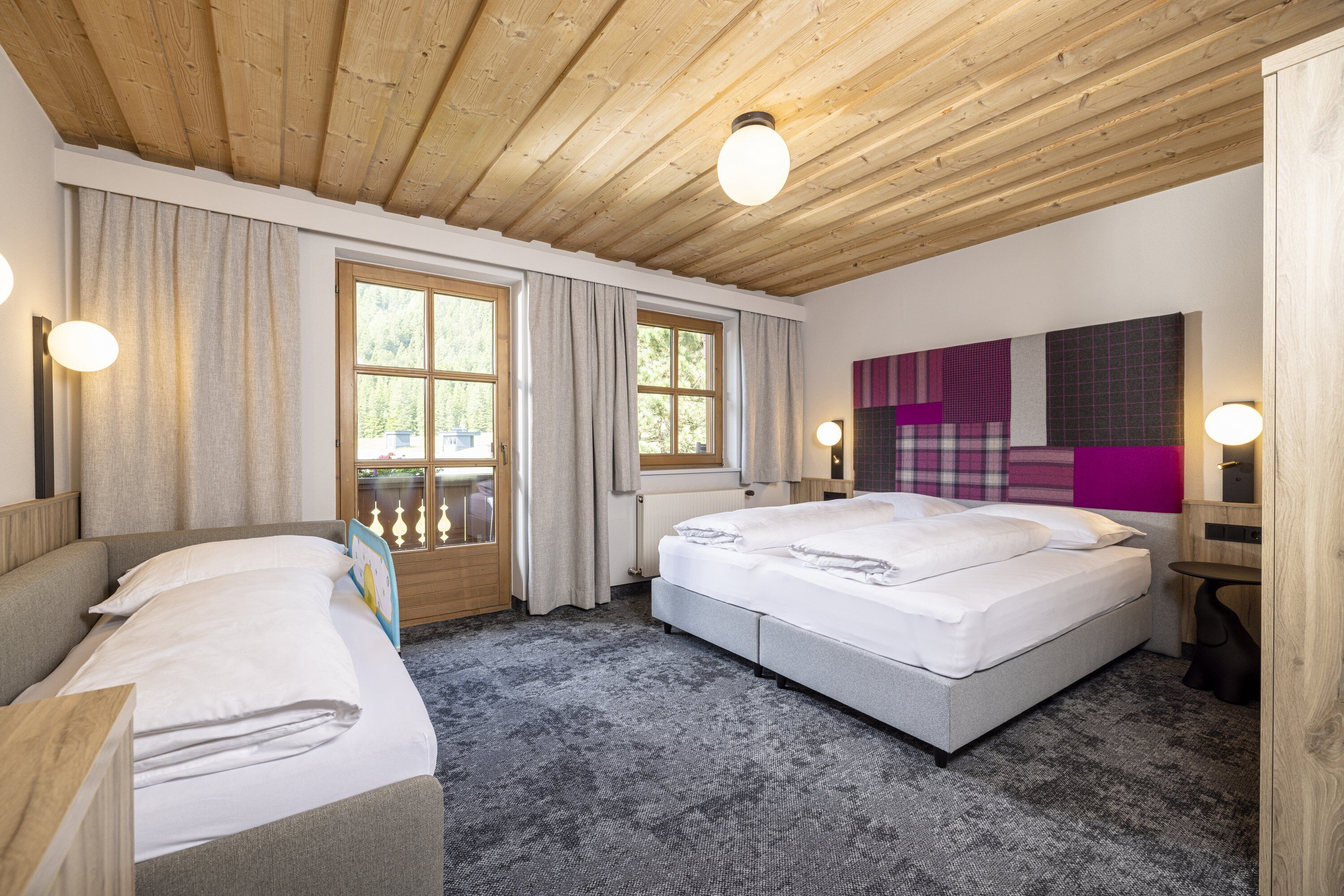 A hotel room with a large bed, a sofa, a window with curtains, and a wooden ceiling.