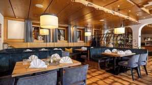 A restaurant with wooden ceiling, blue upholstered booths, and tables set with white napkins and glassware. - Kinder- & Gletscherhotel Hintertuxerhof (Tux)