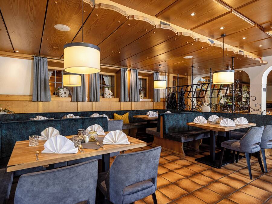A restaurant with wooden ceiling, blue upholstered booths, and tables set with white napkins and glassware.
