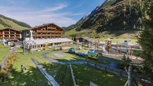 A lodge with a large wooden building, a playground, and a mountain backdrop. - Kinder- & Gletscherhotel Hintertuxerhof (Tux)
