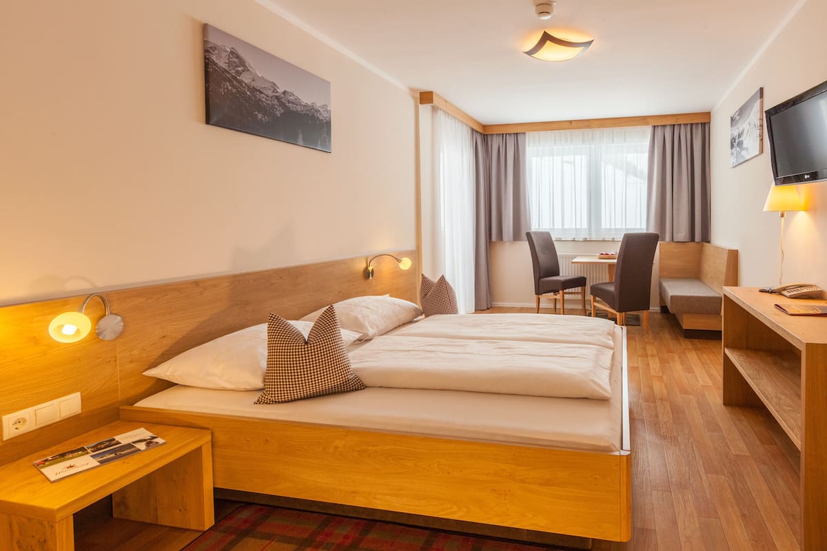 Habitación de hotel con una cama de madera, un escritorio, una silla y un televisor.