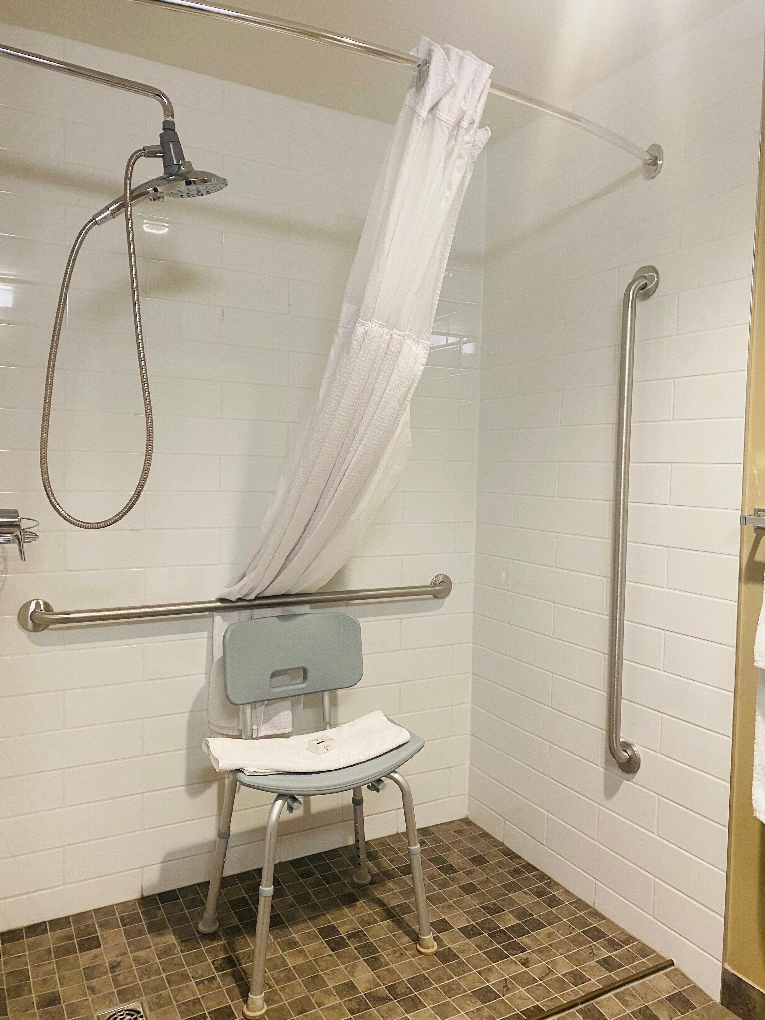 A shower area with a grab bar, a showerhead, and a white shower curtain.