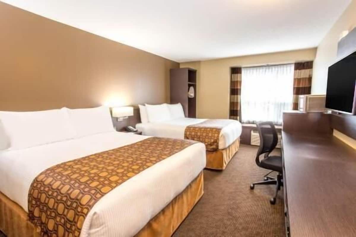 Ein Hotelzimmer mit zwei Betten, einem Schreibtisch, einem Stuhl und einem Fernseher.