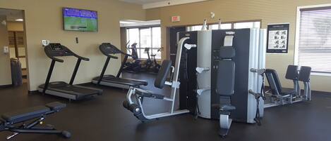 Un gimnasio con cintas de correr, máquinas de pesas y una televisión mostrando un evento deportivo.
