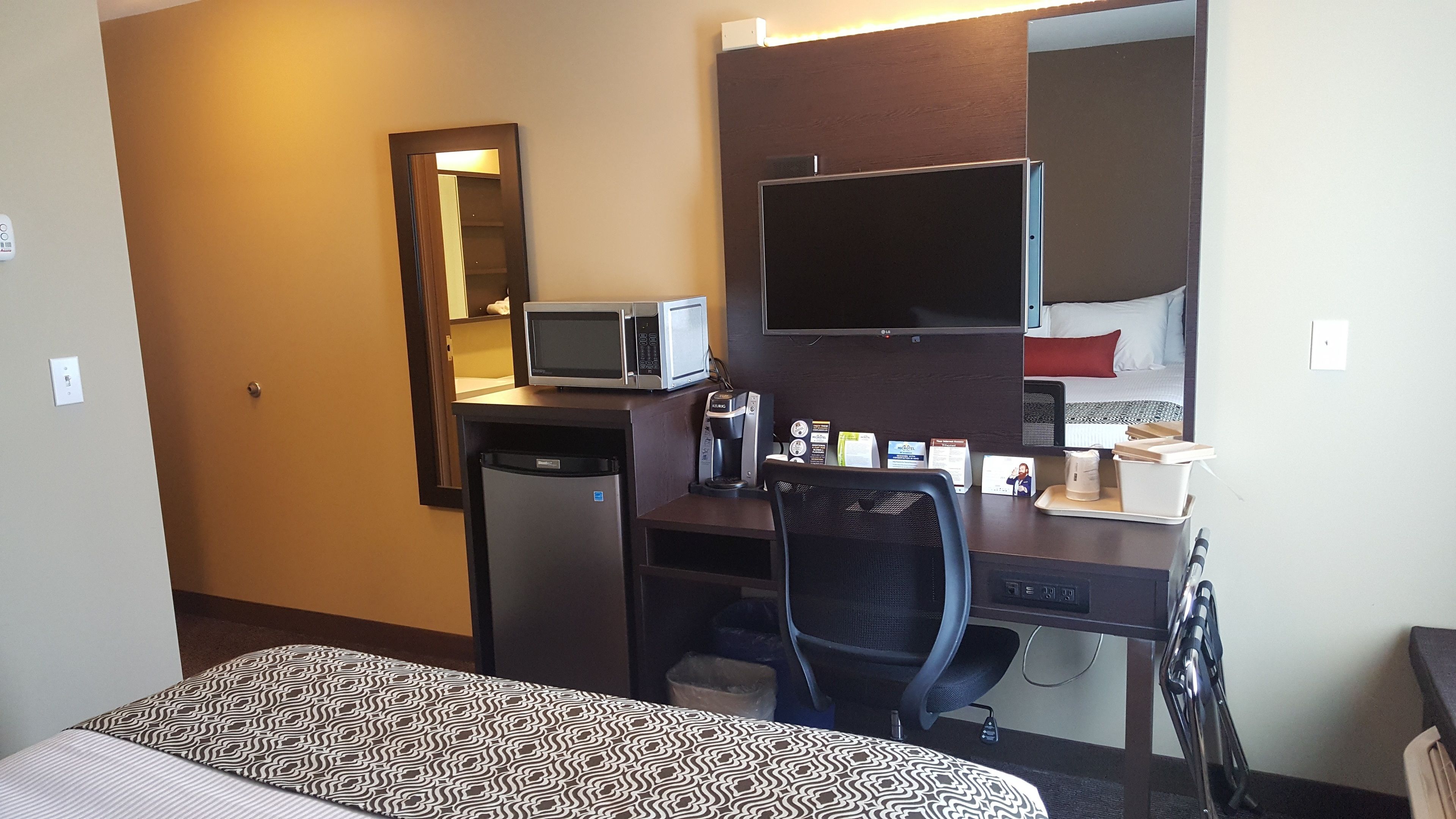 Une chambre d’hôtel équipée d’un lit, d’un bureau avec un ordinateur, d’un four à micro-ondes, d’une machine à café et d’une télévision.