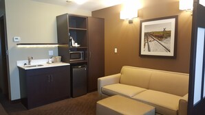 Habitación de hotel compacta con kitchenette, un sofá y un cuadro en la pared.