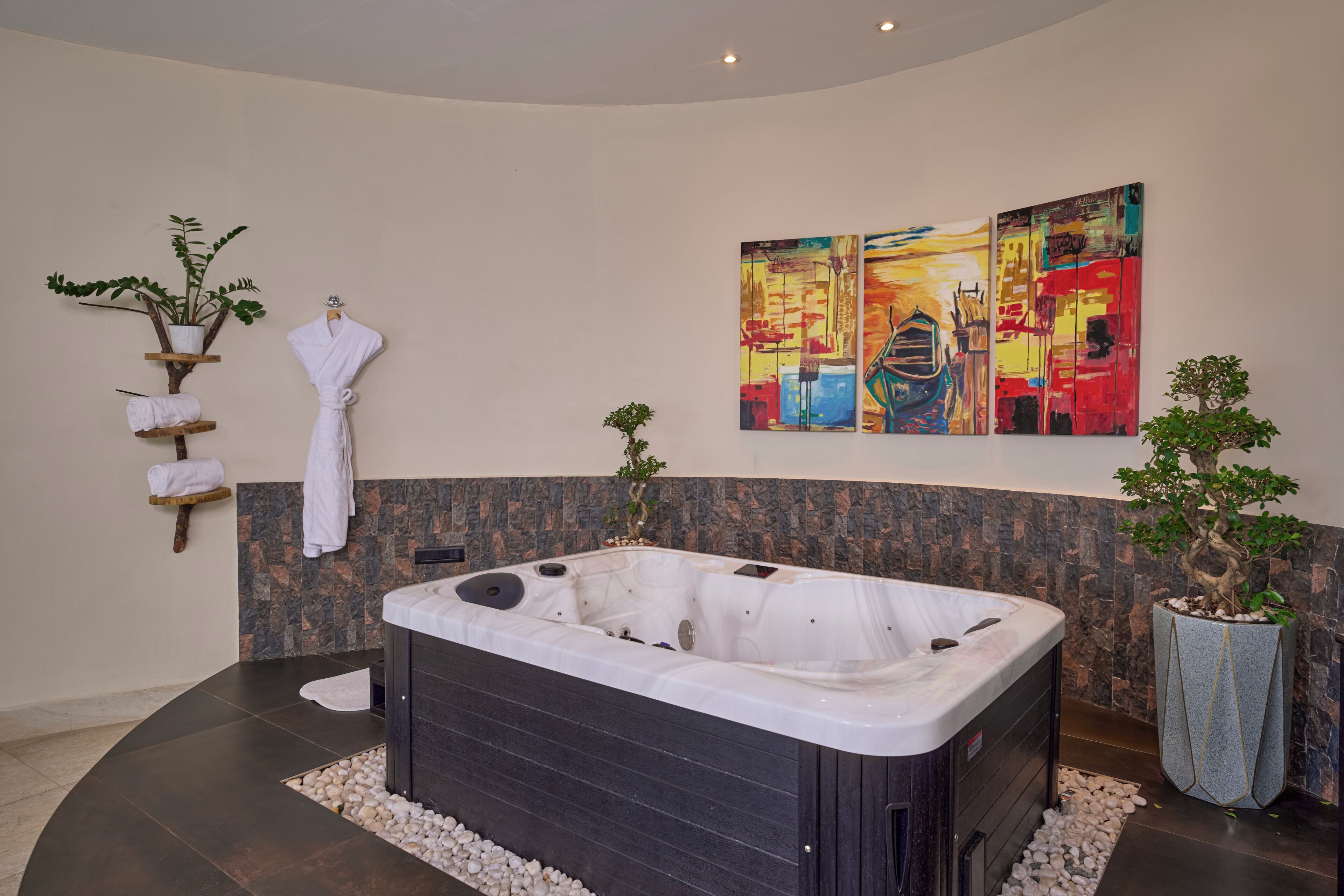 Een moderne badkamer met een bubbelbad, een groot abstract schilderij en twee potplanten.
