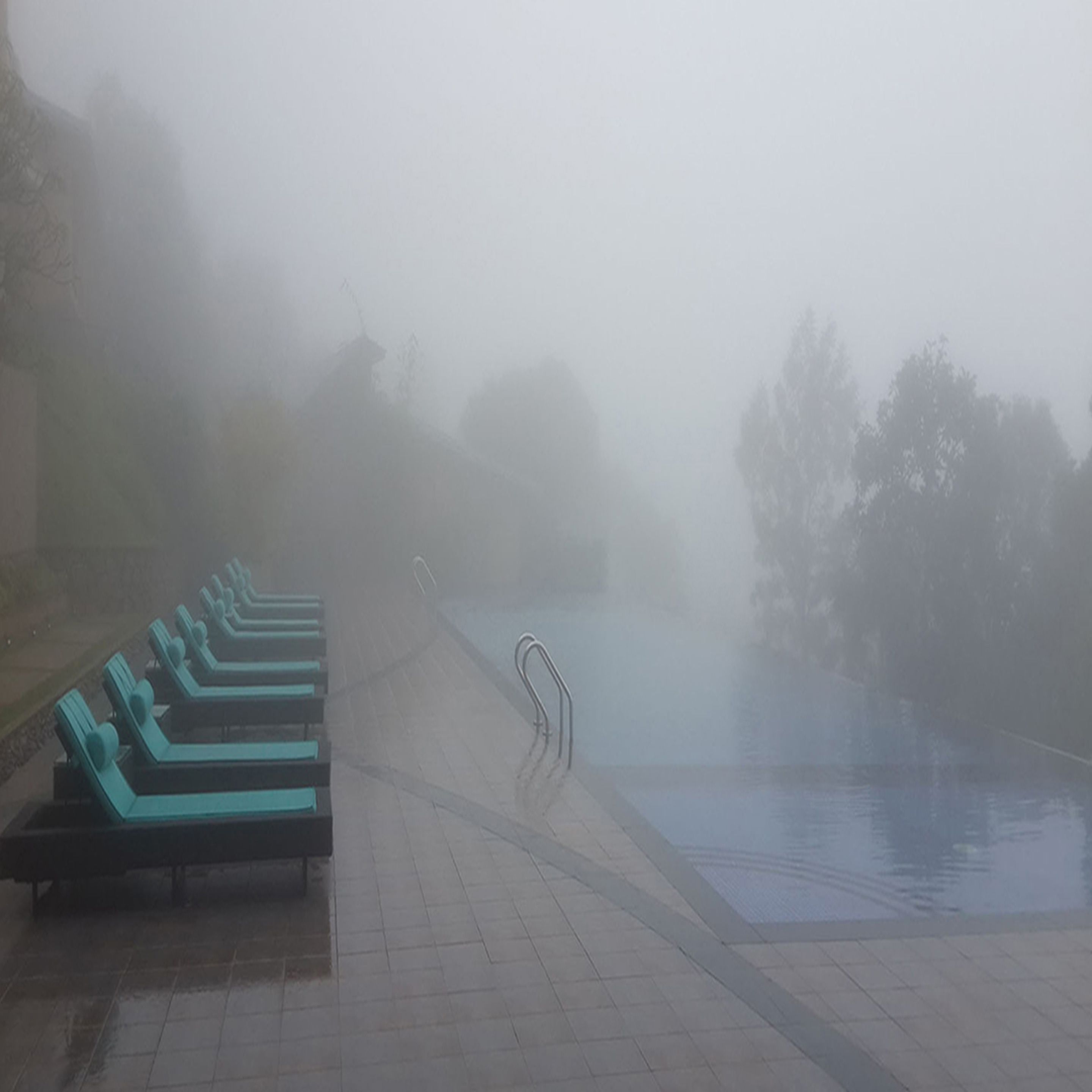 A misty outdoor swimming pool area with lounge chairs and a clear pool.